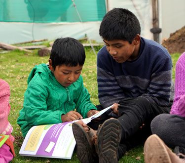 Peruanische Kinder sind über das Bibel-Studienmaterial gebeugt